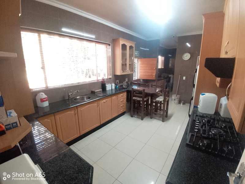 Spacious kitchen featuring granite countertops, wooden cabinetry, gas hob, and tiled finishes, offering a functional layout with ample workspace.