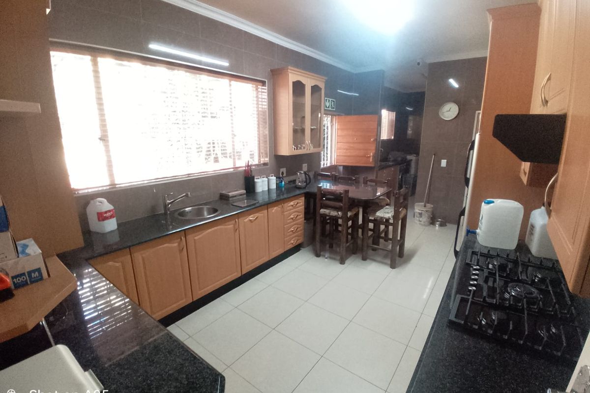 Spacious kitchen featuring granite countertops, wooden cabinetry, gas hob, and tiled finishes, offering a functional layout with ample workspace.