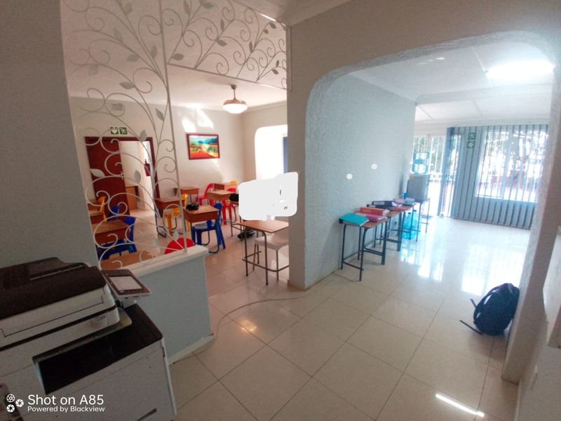 Open plan interior space featuring tiled flooring, an arched transition, and decorative metal screening, currently utilized as a classroom or office area.