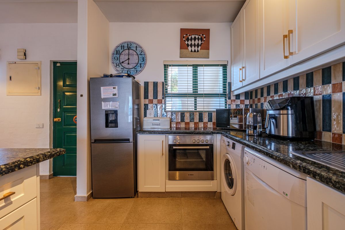 Compact kitchen featuring shaker-style cabinetry, granite countertops, tiled backsplash, and built-in appliances including an oven, washing machine, and dishwasher.