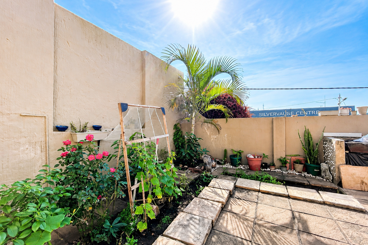 A private rear courtyard featuring a paved patio area, boundary walls, and established garden beds with integrated planters.