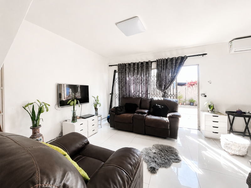 A bright living room featuring polished tile flooring, a wall-mounted air conditioning unit, and direct access to an outdoor patio area through a sliding door.