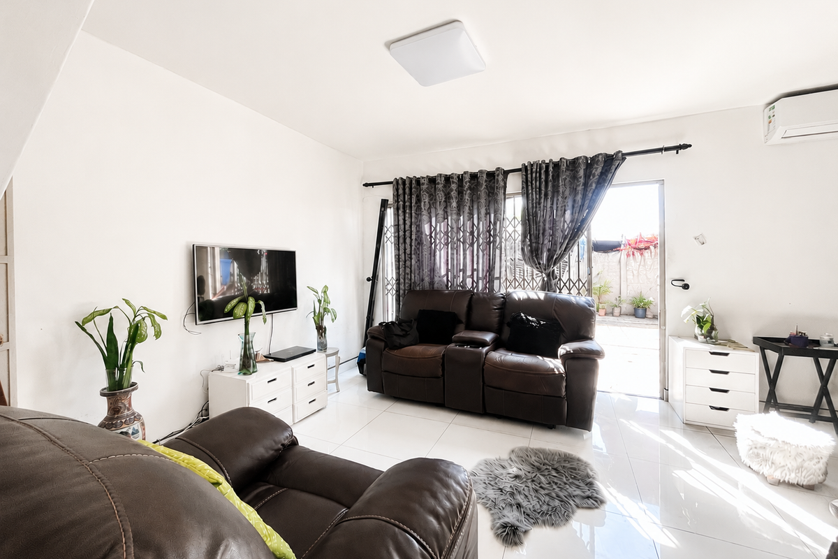 A bright living room featuring polished tile flooring, a wall-mounted air conditioning unit, and direct access to an outdoor patio area through a sliding door.