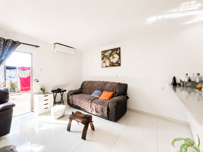 Open plan living area featuring tiled flooring, a wall-mounted air conditioning unit, and direct access to an outdoor patio space.