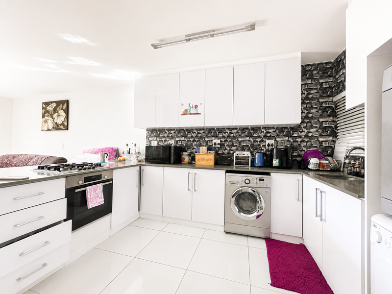 Modern kitchen featuring white cabinetry, built-in oven, gas hob, and integrated washing machine with a distinctive textured splashback and tiled flooring.