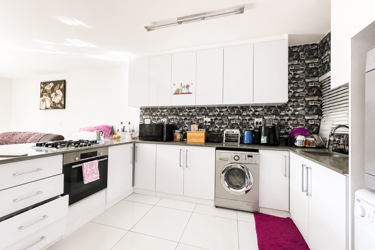 Modern kitchen featuring white cabinetry, built-in oven, gas hob, and integrated washing machine with a distinctive textured splashback and tiled flooring.