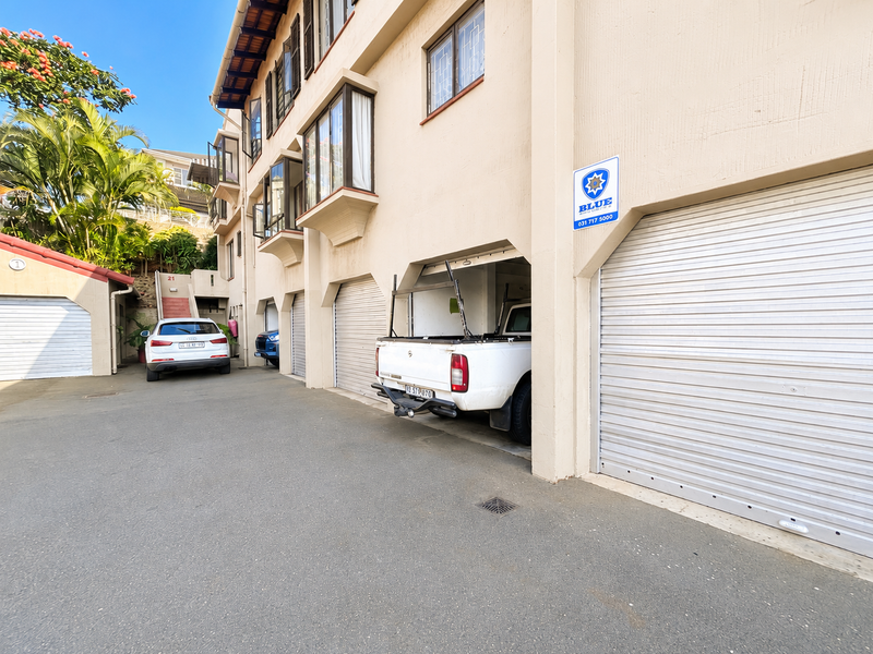 Exterior view of a multi-unit apartment complex featuring multiple individual roller shutter garage doors and paved driveway access.