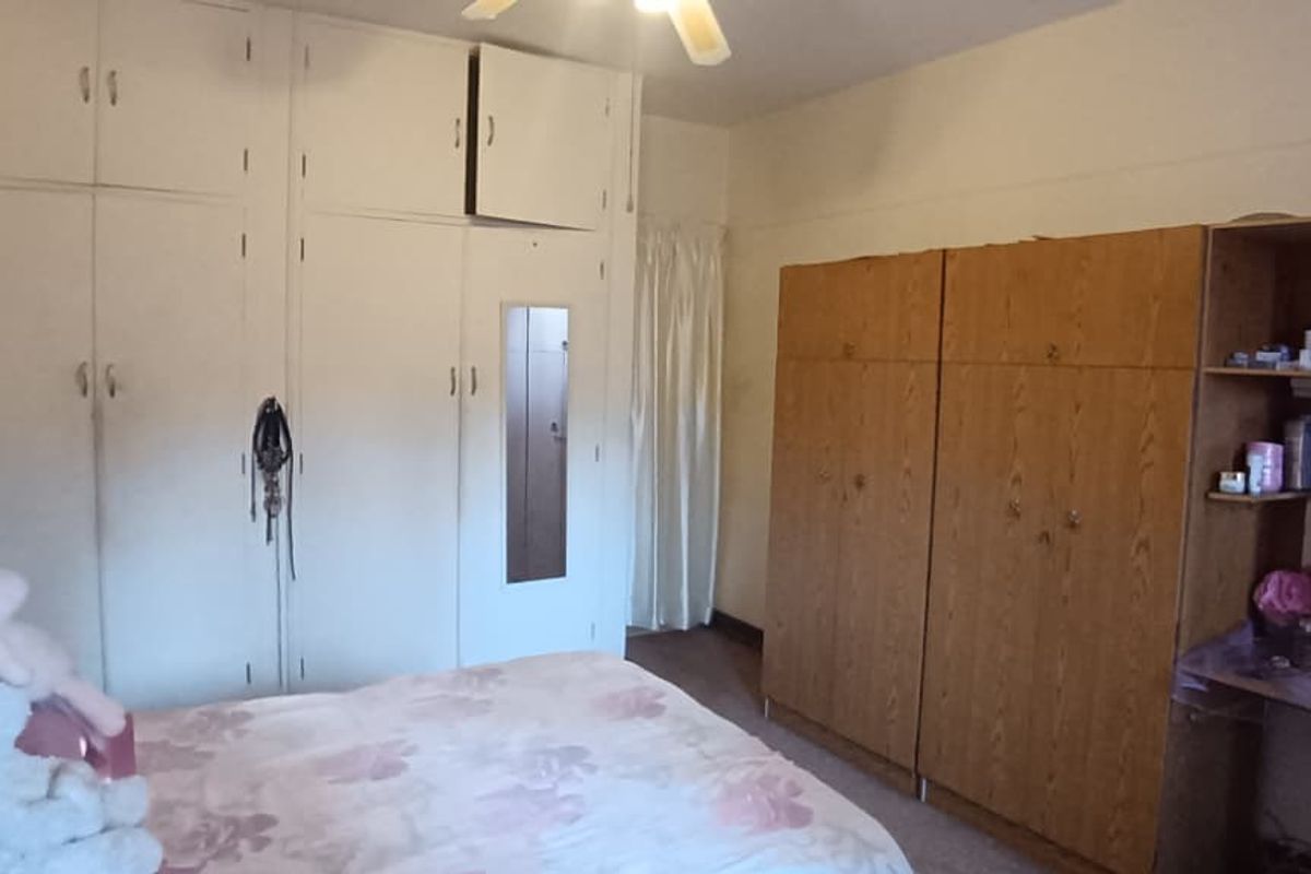 Bedroom featuring extensive built-in wardrobe storage and a ceiling fan, requiring cosmetic updates to modernize the dated cabinetry and finishes.