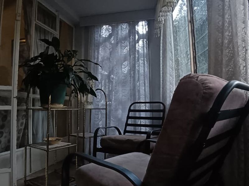Enclosed patio or sunroom featuring metal-framed glass doors and louvre windows, offering a dated but functional space for relaxation.