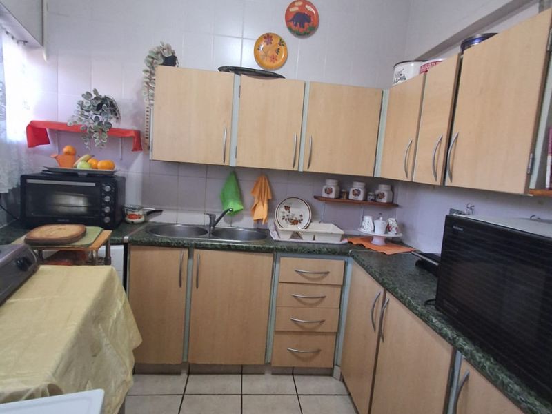 A functional kitchen featuring light wood-tone cabinetry, laminate countertops, a double bowl sink, and tiled flooring with a neutral tiled splashback.