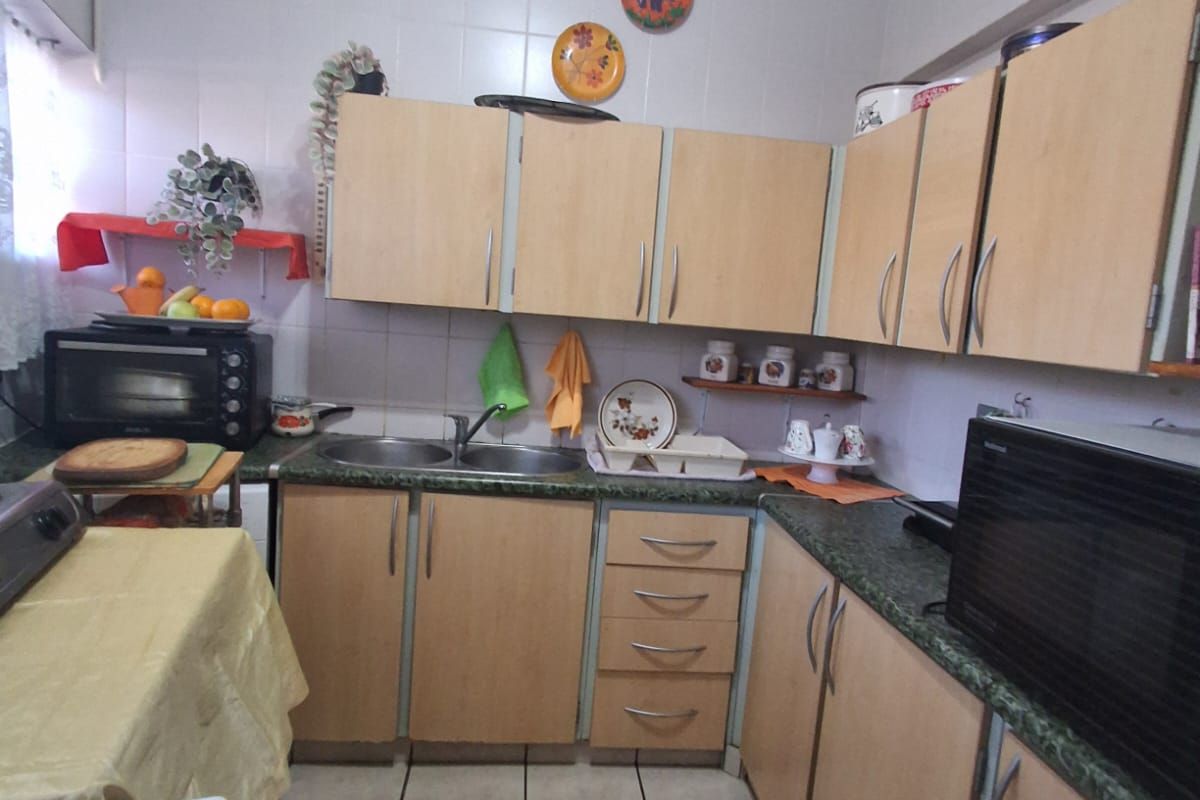 A functional kitchen featuring light wood-tone cabinetry, laminate countertops, a double bowl sink, and tiled flooring with a neutral tiled splashback.