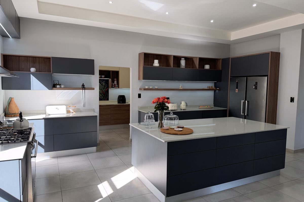 Modern kitchen featuring a large central island, sleek dark cabinetry, quartz countertops, and high-end integrated appliances, with an adjacent scullery area.