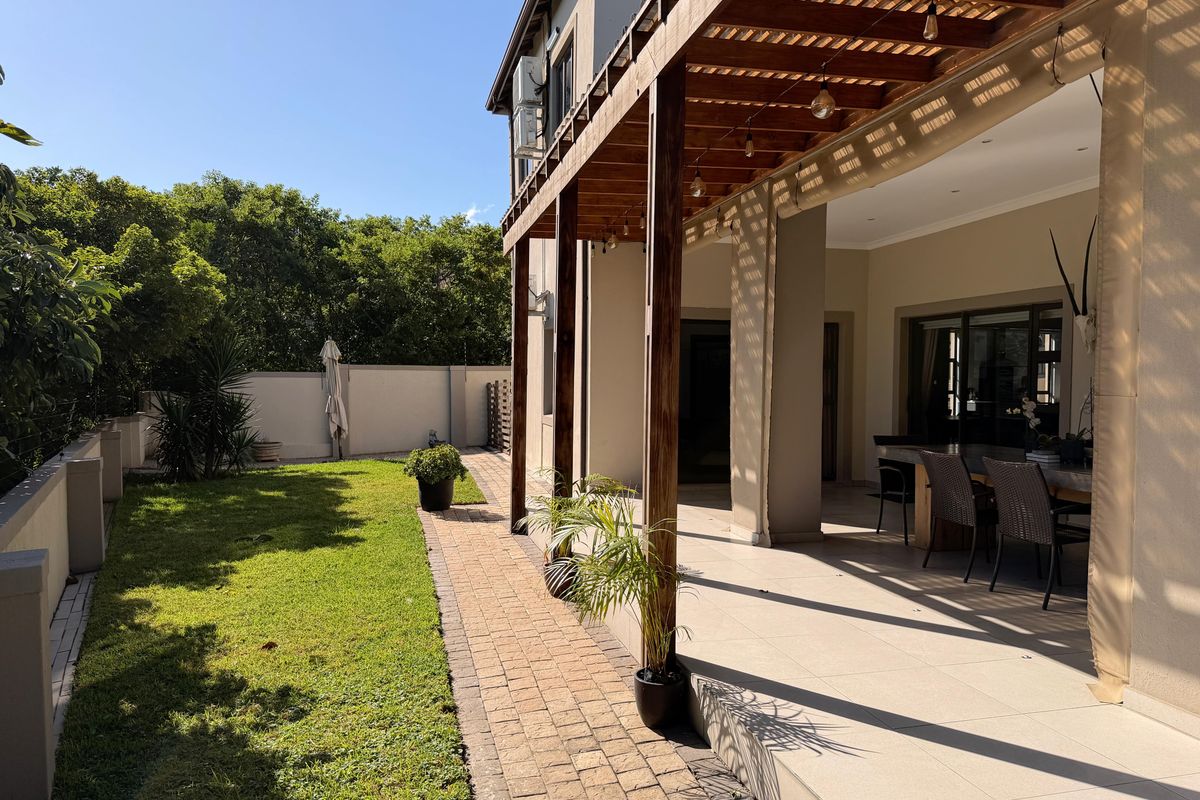 A well-maintained rear exterior featuring a covered timber pergola patio, tiled flooring, and a neat garden with a paved walkway.