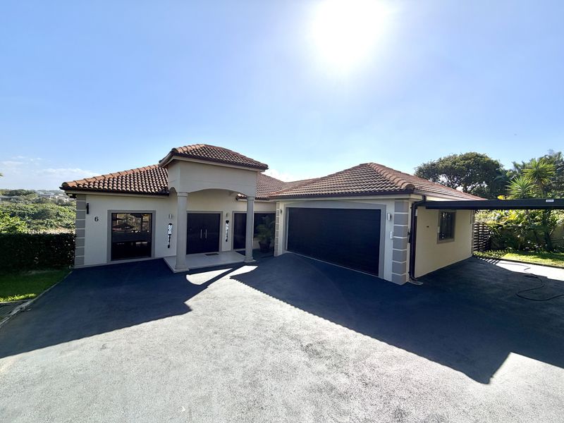 Front elevation of a well-maintained residence featuring a tiled roof, covered entrance with pillars, and a spacious paved driveway leading to a double garage.