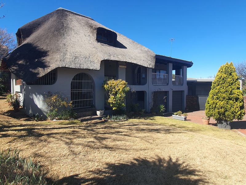 Front view of a two-story house featuring a traditional thatch roof, a paved driveway, and a balcony overlooking the front garden.