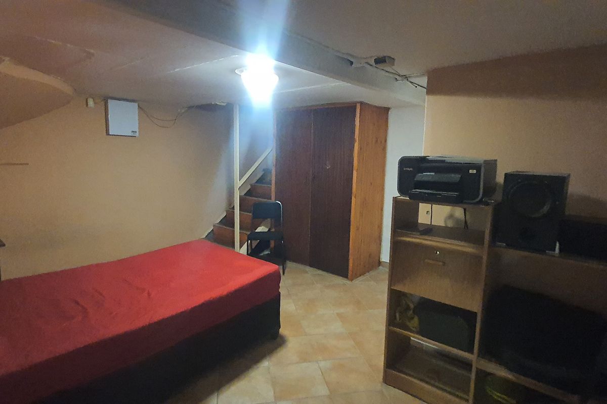 A basement-level bedroom featuring tiled flooring, a built-in wooden wardrobe, and an integrated staircase, requiring cosmetic updates to improve the overall finish.