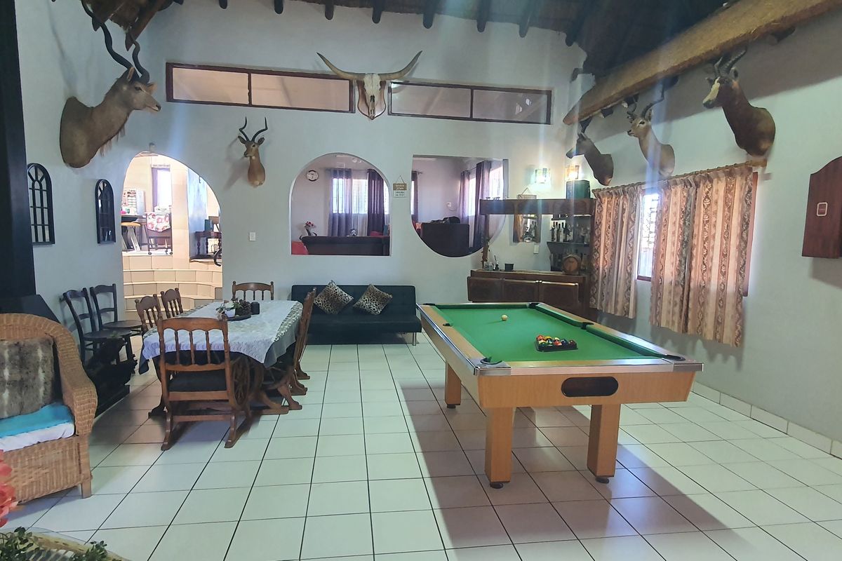 Spacious open-plan living area featuring tiled floors, an exposed beam thatched ceiling, a freestanding fireplace, and a built-in bar area.