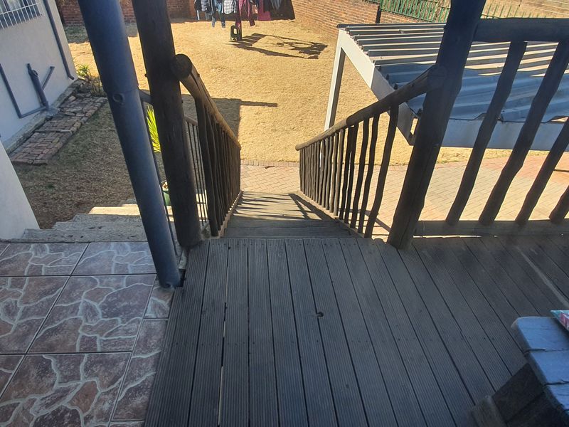An elevated timber deck with a staircase leading down to the rear garden area, featuring a pergola and tiled transition section.