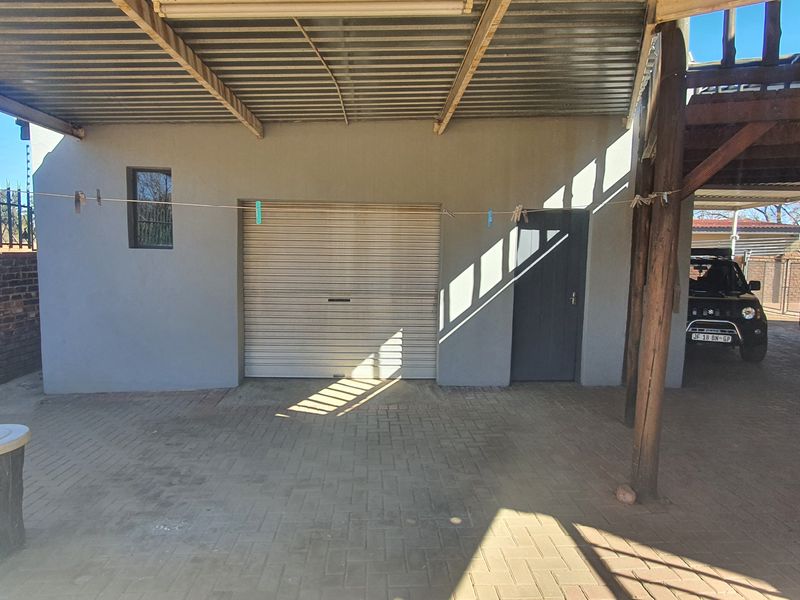 A functional garage area featuring a roller shutter door, covered parking space, and secure brick boundary wall with electric fencing.