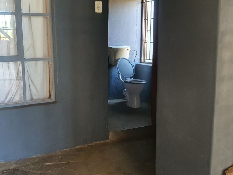 A small, functional bathroom space featuring a standard toilet, security bars on the window, and stone flooring.