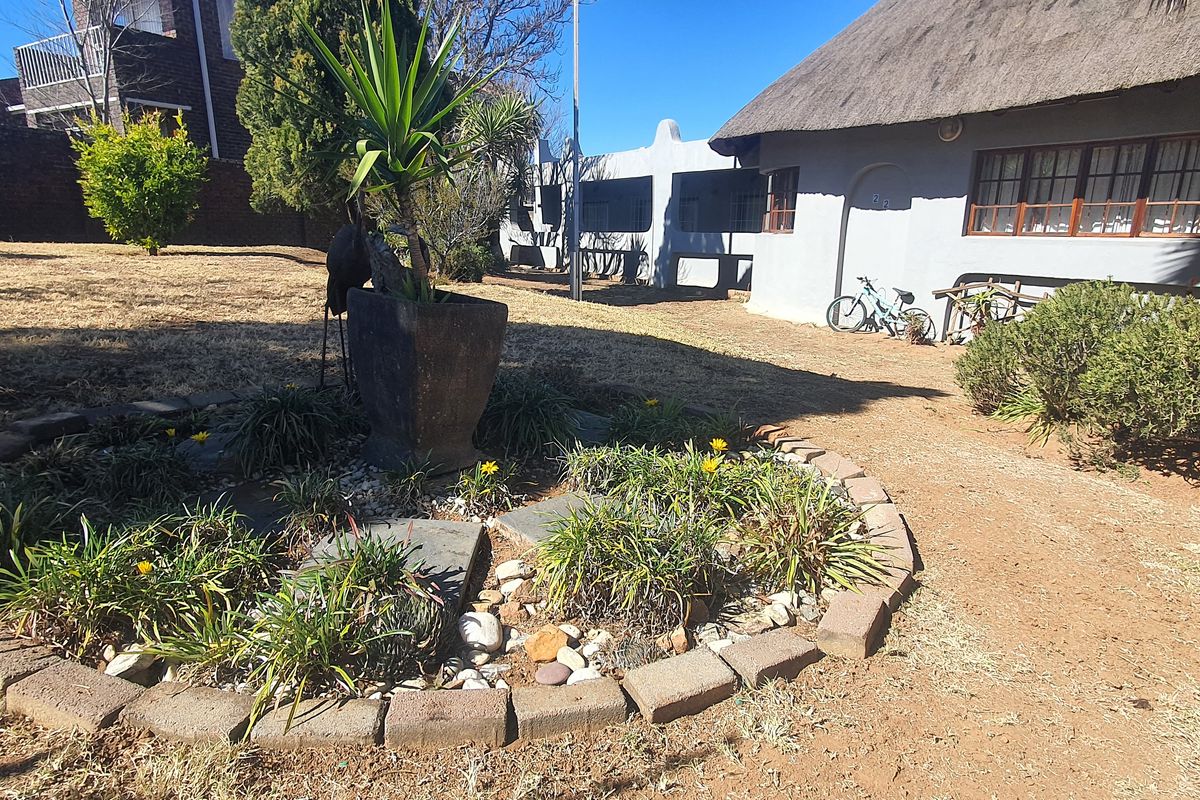 Rear garden area featuring a thatched roof dwelling with brick-edged landscaping and a large open yard space.