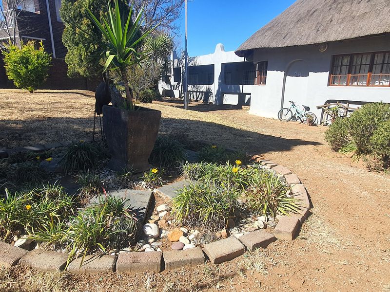 Rear garden area featuring a thatched roof dwelling with brick-edged landscaping and a large open yard space.