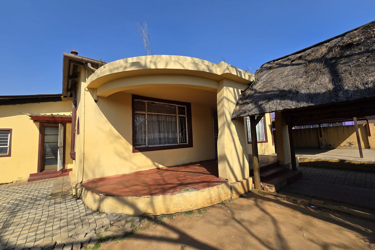 Rear exterior view of the house featuring a curved covered patio, terracotta tiling, and an adjacent thatched roof structure requiring maintenance.