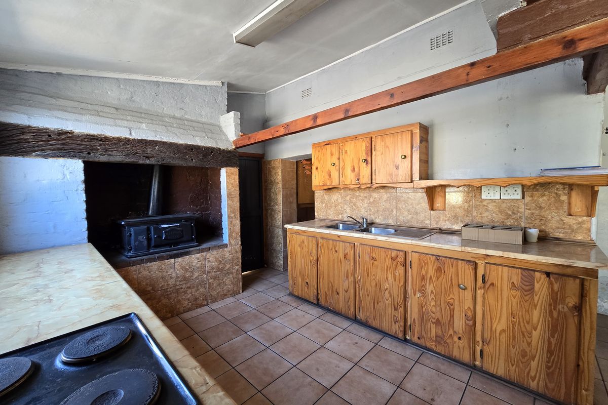 A rustic kitchen featuring wooden cabinetry, tiled surfaces, and a built-in fireplace, offering a dated aesthetic with potential for modern renovation.