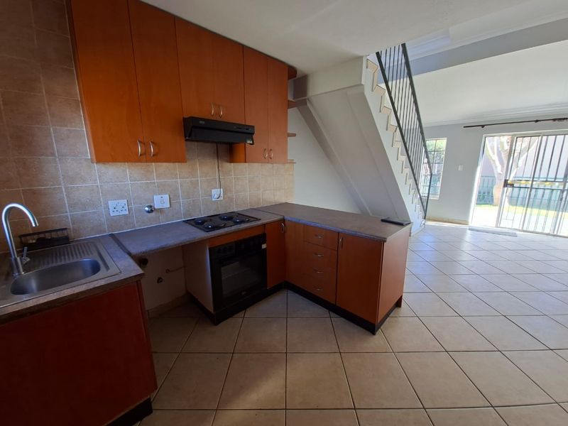 Open-plan kitchen and living area featuring wood-finish cabinetry, built-in appliances, tiled flooring, and direct access to the rear exterior via a sliding door.