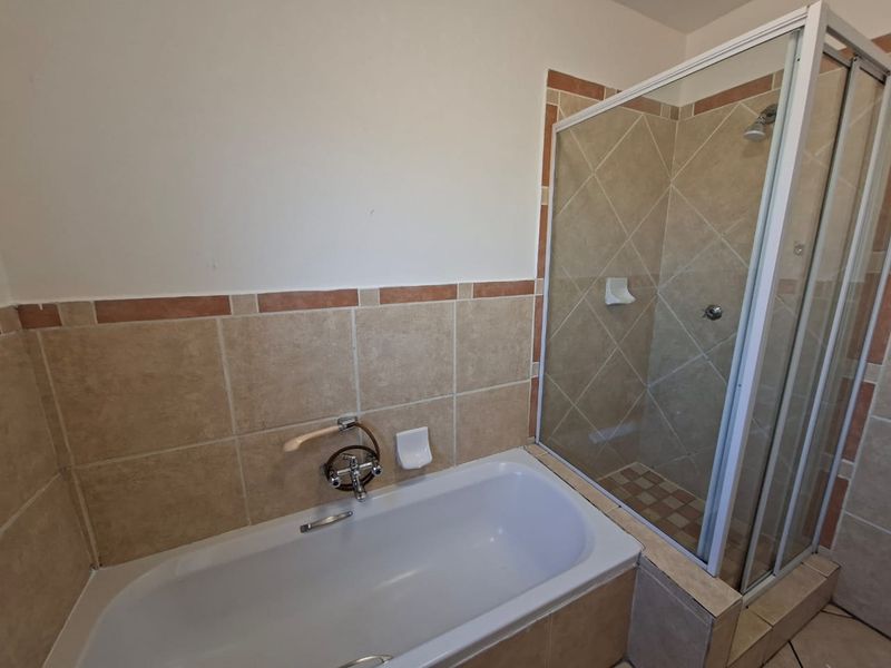 A functional bathroom featuring a built-in bathtub and a separate glass-enclosed shower with neutral ceramic tiling.