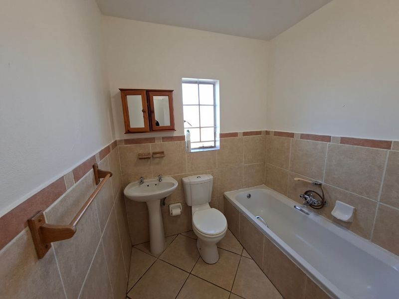 A functional bathroom featuring a pedestal basin, toilet, and bathtub with neutral wall and floor tiling.