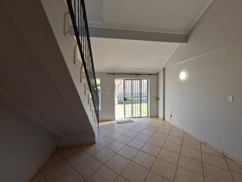An empty, open-plan living area featuring tiled flooring, a staircase with a metal balustrade, and a sliding glass door leading to the exterior.