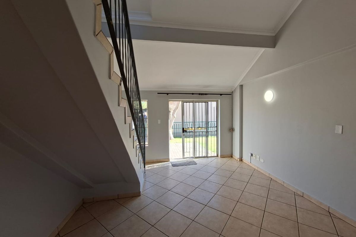 An empty, open-plan living area featuring tiled flooring, a staircase with a metal balustrade, and a sliding glass door leading to the exterior.