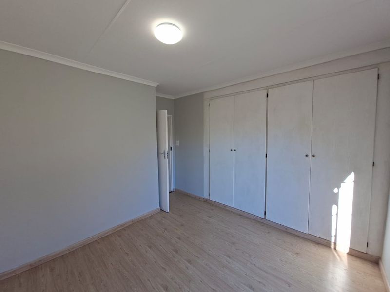A clean, empty bedroom featuring light-toned laminate flooring and ample built-in cupboard storage space.