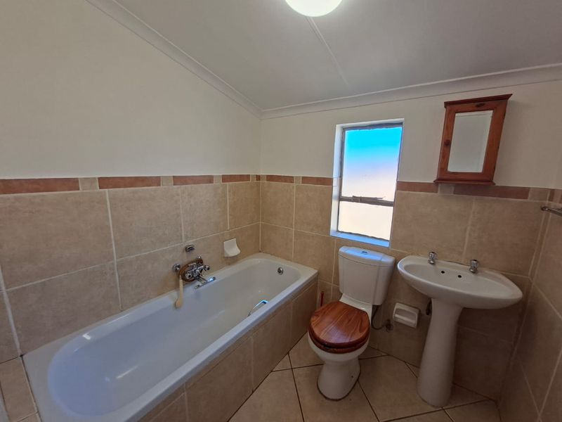 A functional bathroom featuring a bathtub, pedestal basin, and toilet with neutral wall and floor tiling.