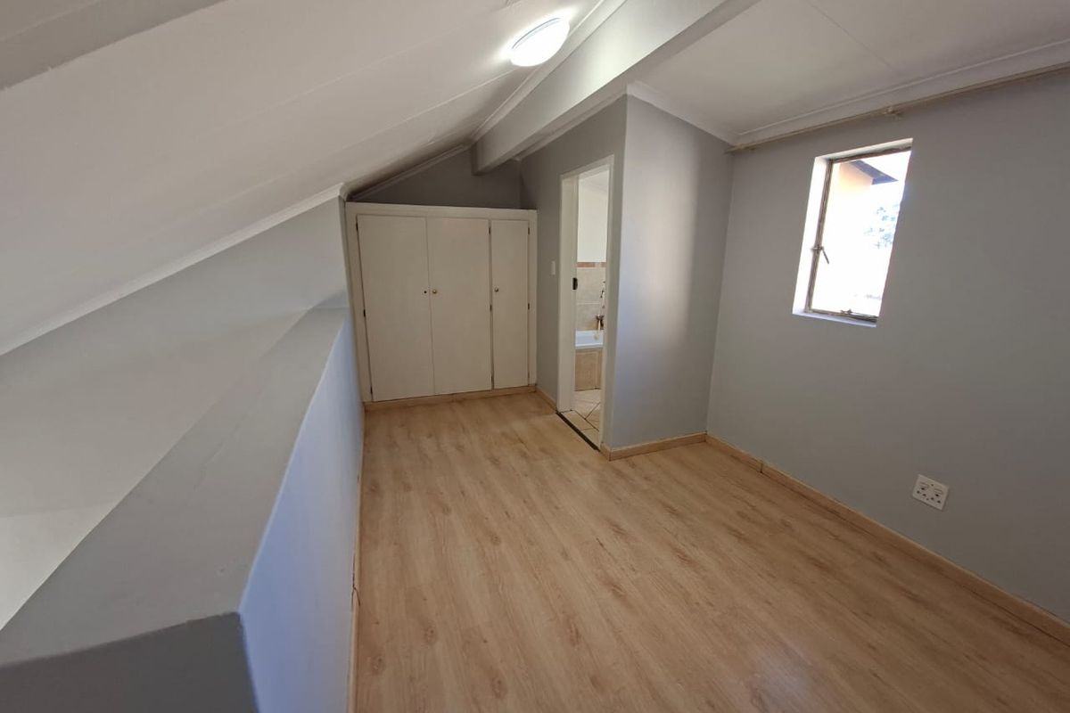 An empty bedroom featuring laminate flooring, sloped ceilings, and built-in cupboards, with an adjoining bathroom visible through the doorway.