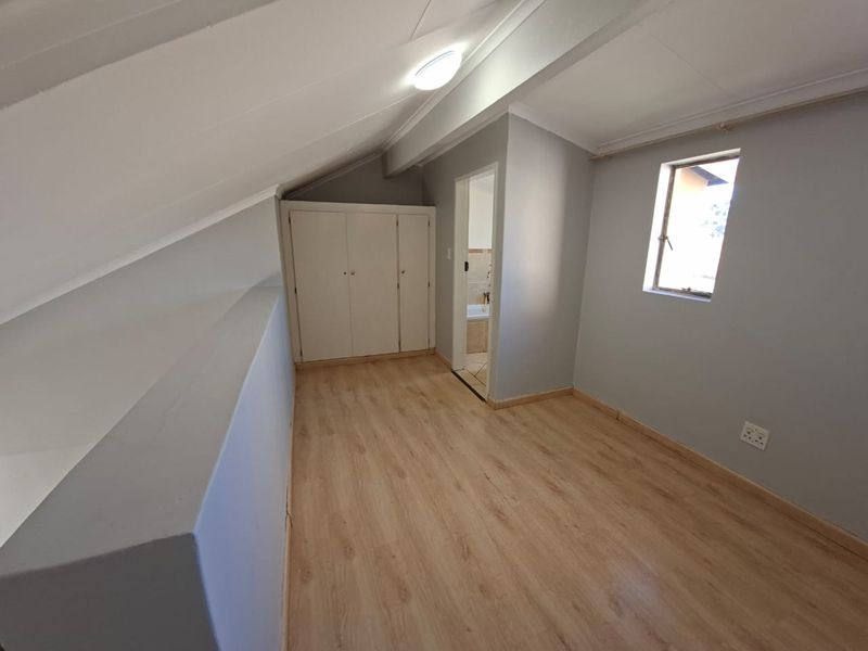 An empty bedroom featuring laminate flooring, sloped ceilings, and built-in cupboards, with an adjoining bathroom visible through the doorway.