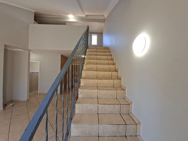 An empty hallway featuring a tiled staircase with a metal balustrade, leading to an upper level with neutral wall finishes.