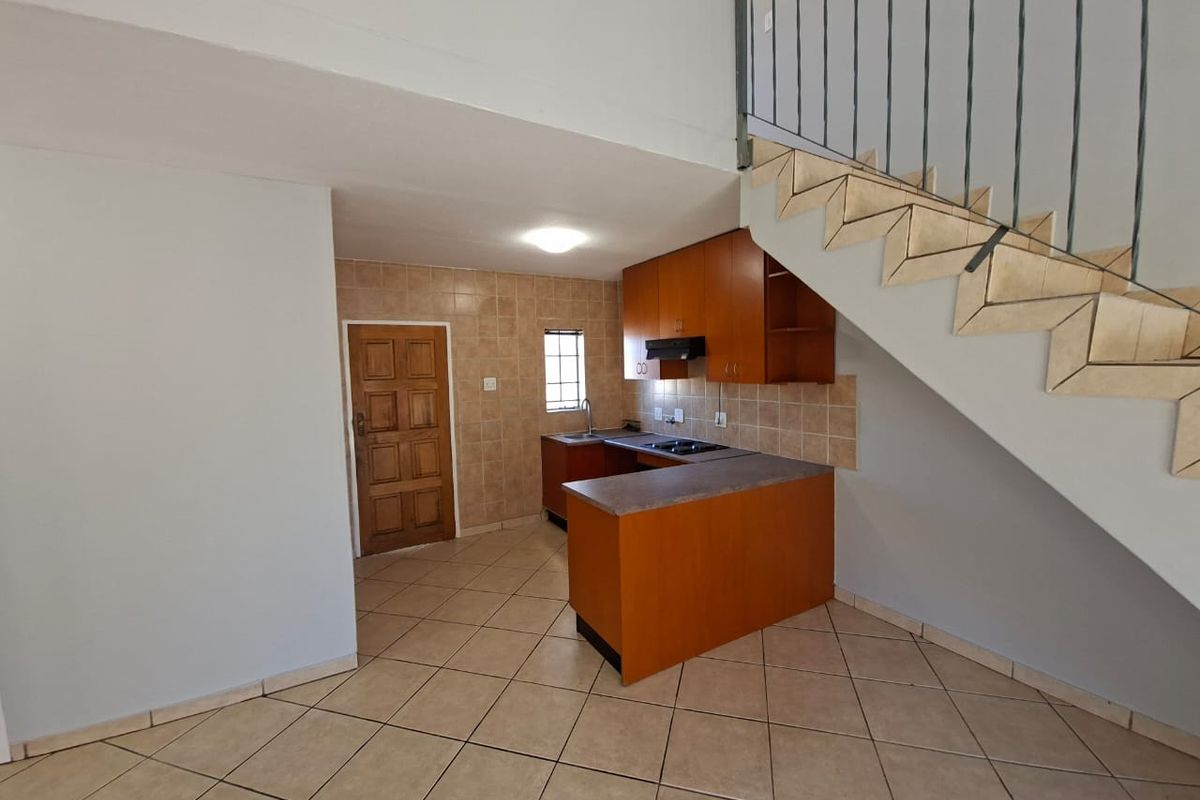 Compact kitchen featuring built-in wooden cabinetry, laminate countertops, and tiled finishes, conveniently located beneath the staircase in an open-plan living area.