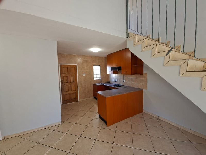 Compact kitchen featuring built-in wooden cabinetry, laminate countertops, and tiled finishes, conveniently located beneath the staircase in an open-plan living area.