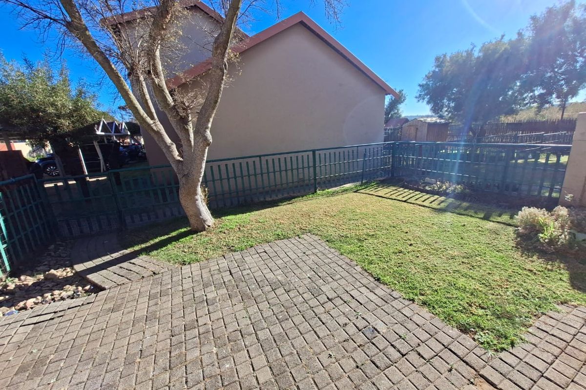 A private rear garden featuring a paved patio area, established lawn, and secure metal perimeter fencing.