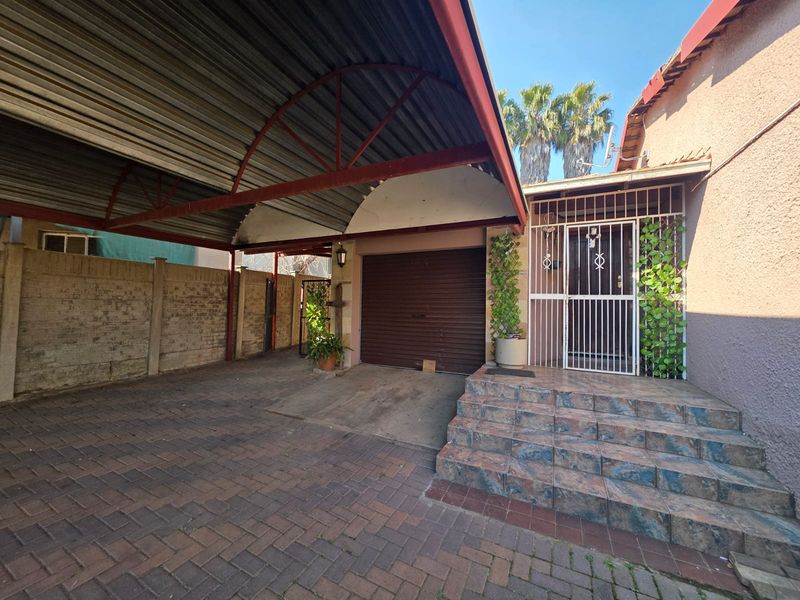 Front entrance area featuring a covered carport, paved driveway, and tiled steps leading to a secure entrance door.