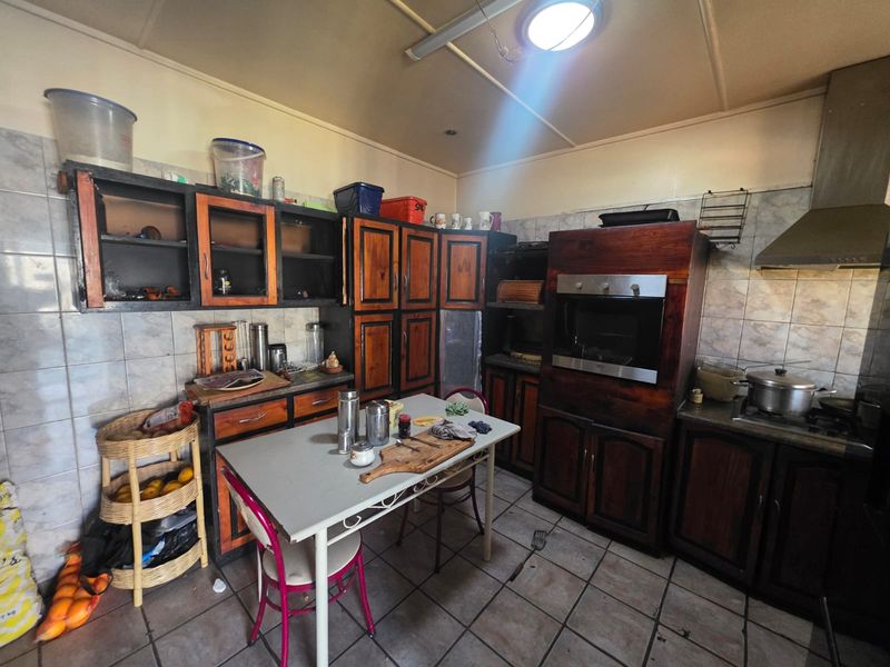 A dated kitchen featuring dark wood cabinetry, built-in oven, extractor fan, and tiled flooring, offering significant potential for a modern renovation.