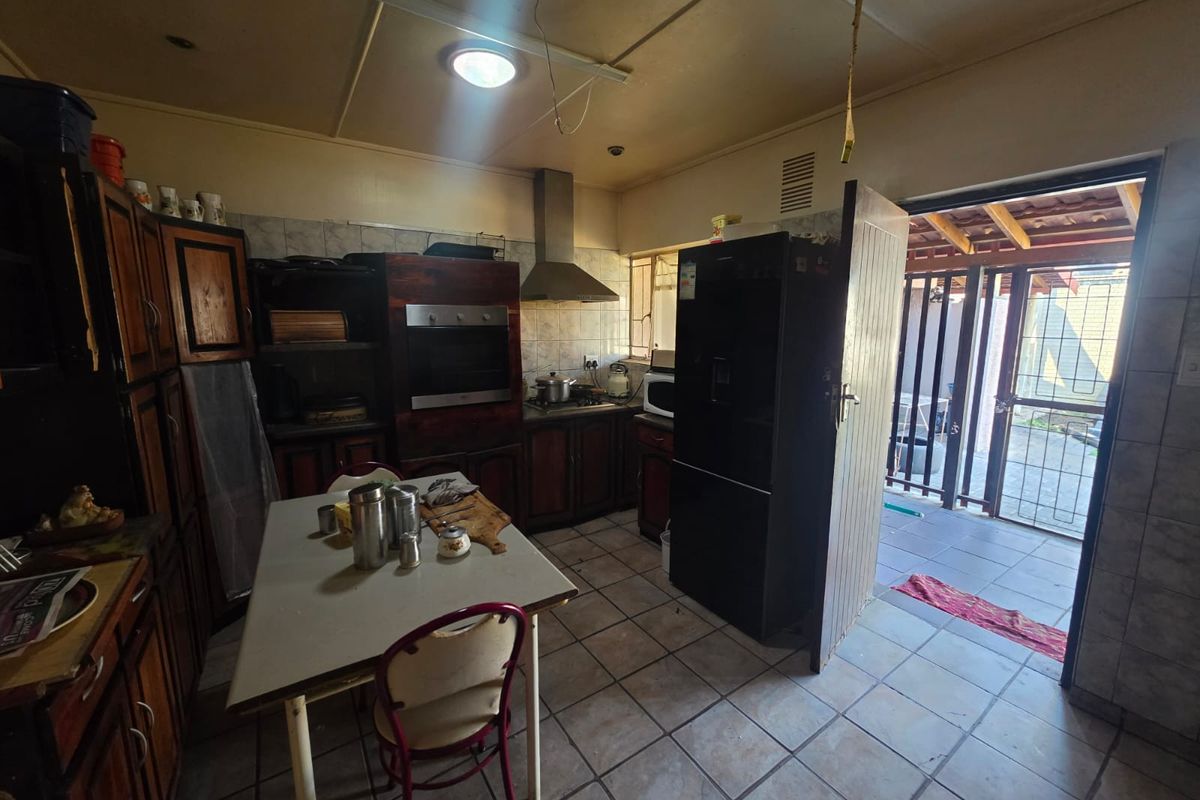 A dated kitchen featuring wooden cabinetry, built-in oven, and extractor fan, with direct access to an outdoor patio area through a security gate.