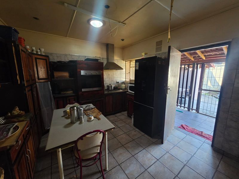 A dated kitchen featuring wooden cabinetry, built-in oven, and extractor fan, with direct access to an outdoor patio area through a security gate.