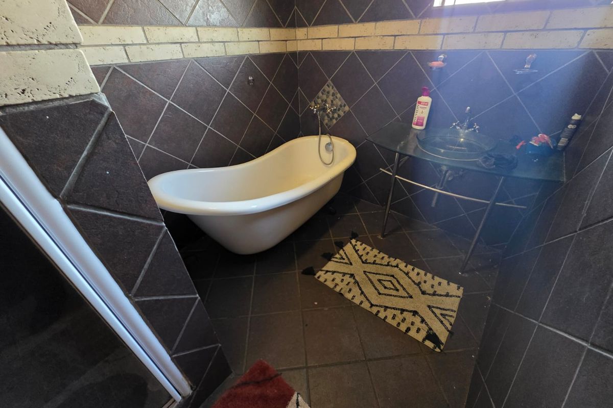 A bathroom featuring a freestanding bathtub, a glass vessel sink with a metal stand, and dark ceramic wall and floor tiling.