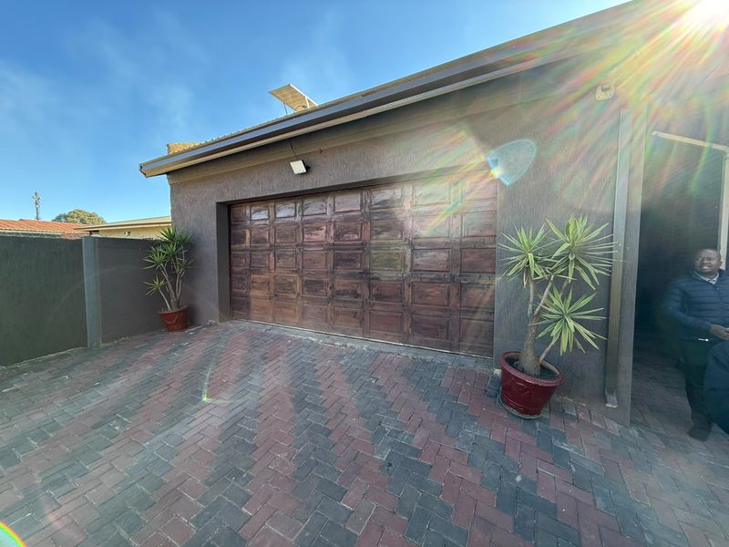A secure garage featuring a wooden sectional door and a paved driveway, equipped with external lighting and a roof-mounted solar panel.