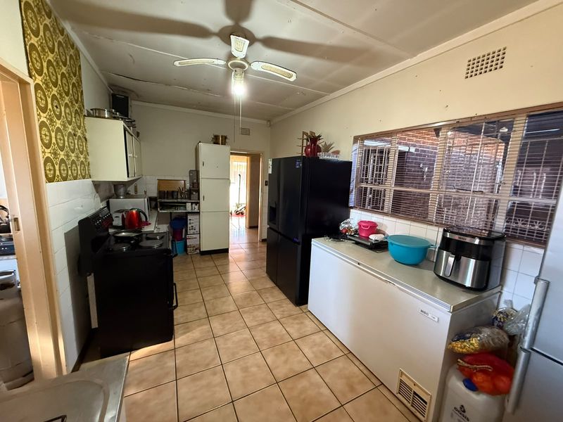 A functional kitchen featuring tiled flooring, built-in cabinetry, and a ceiling fan, currently requiring cosmetic updates to modernize the space.