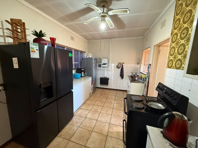 A functional kitchen featuring tiled flooring, a ceiling fan, and a tiled splashback, offering a practical layout with ample space for appliances.