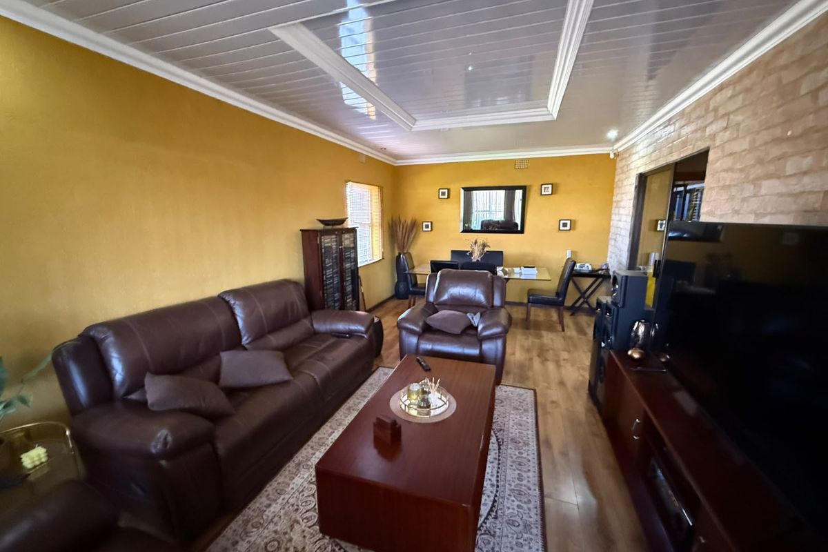 A living room featuring laminate flooring, an exposed brick feature wall, and a recessed ceiling panel with coved cornice detailing.